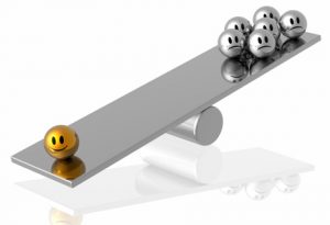 A silver seesaw with a gold smiley face on one side and several silver frowning faces on the other side.
