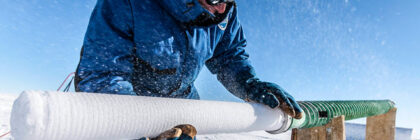 Scientist in winter gear extracting an ice core sample from a snowy environment.