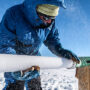 Scientist in winter gear extracting an ice core sample from a snowy environment.
