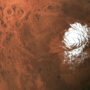 Aerial view of a white ice cap on the surface of Mars surrounded by reddish terrain and craters.