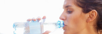 Woman taking a sip from a clear plastic water bottle outdoors in natural light.